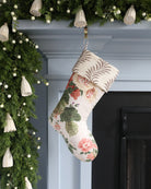Floral-patterned Christmas stocking hanging on a fireplace with greenery and lights.